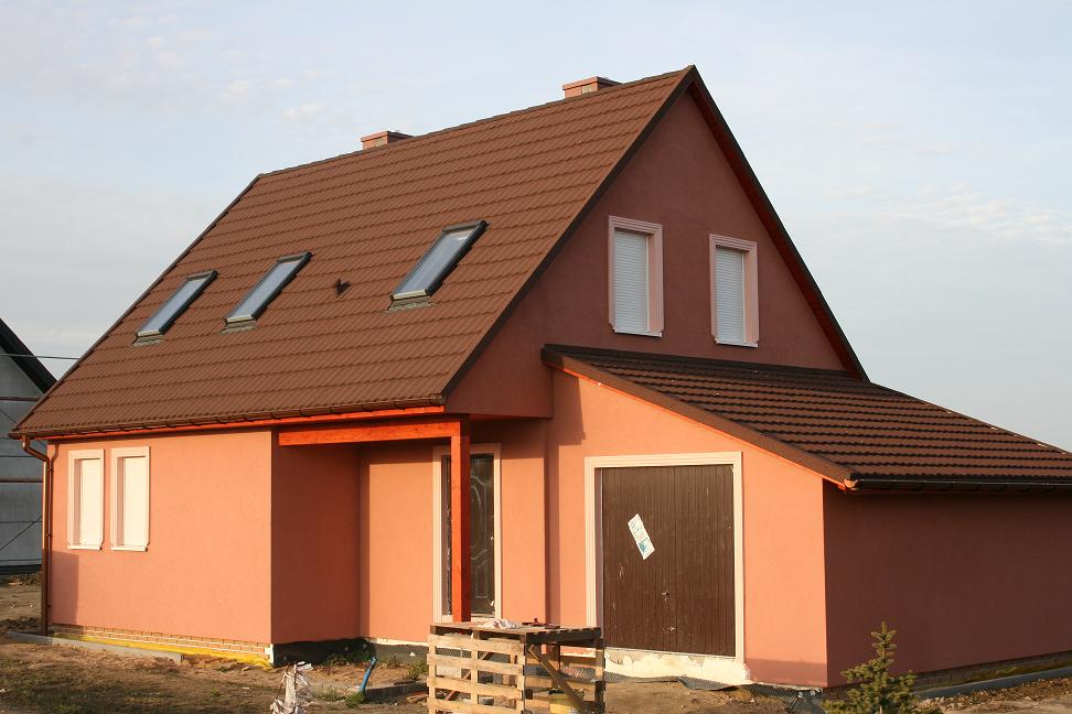 Niedawno wybudowany dom w stanie deweloperskim z brązową dachówką, oknami dachowymi i garażem, z paletą na pierwszym planie.