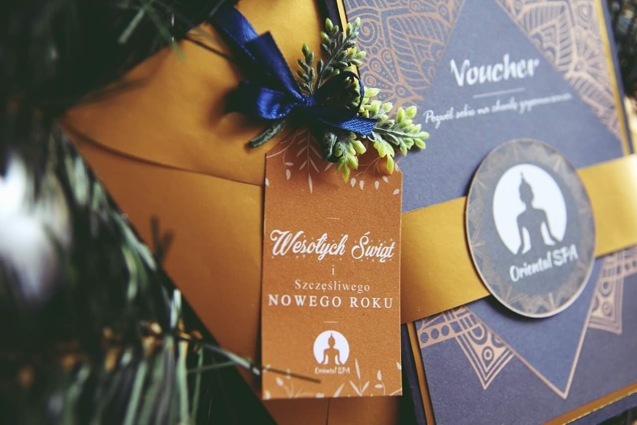 Elegancki, świąteczny voucher SPA z granatowo-złotym motywem, przewiązany niebieską wstążką i ozdobiony gałązką, z zawieszką z życzeniami 'Wesołych Świąt i Szczęśliwego Nowego Roku'.