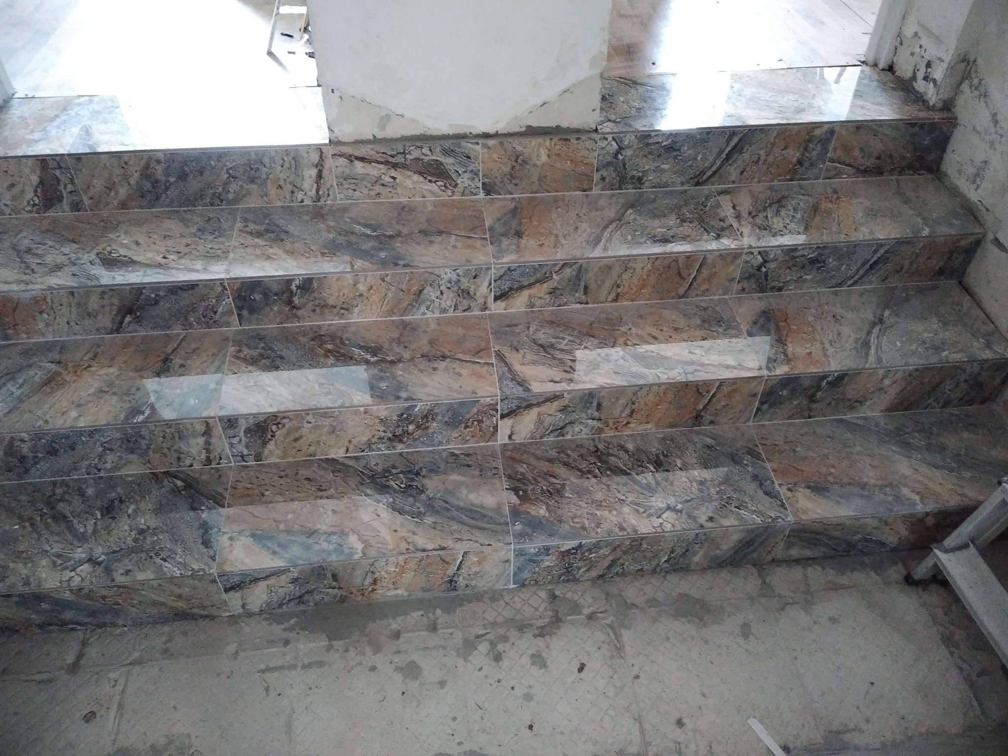 Wyłożone marmurkowymi płytkami schody w trakcie prac wykończeniowych, widoczne niedociągnięcia na ścianie i podłodze.