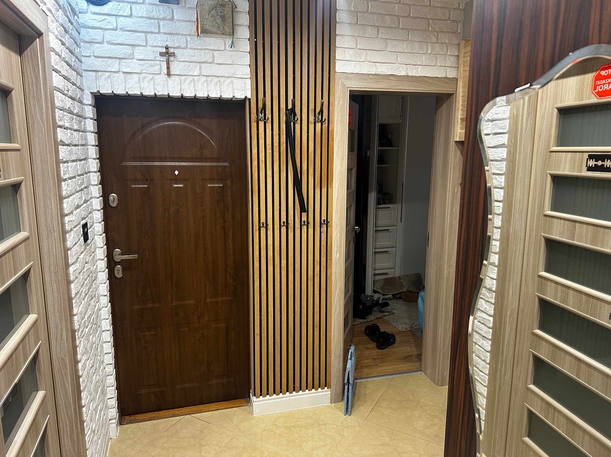 Nowoczesny przedpokój z drewnianym panelem ściennym, wieszakami i dwiema parami drzwi. Biała cegła na ścianie dodaje wnętrzu charakteru.