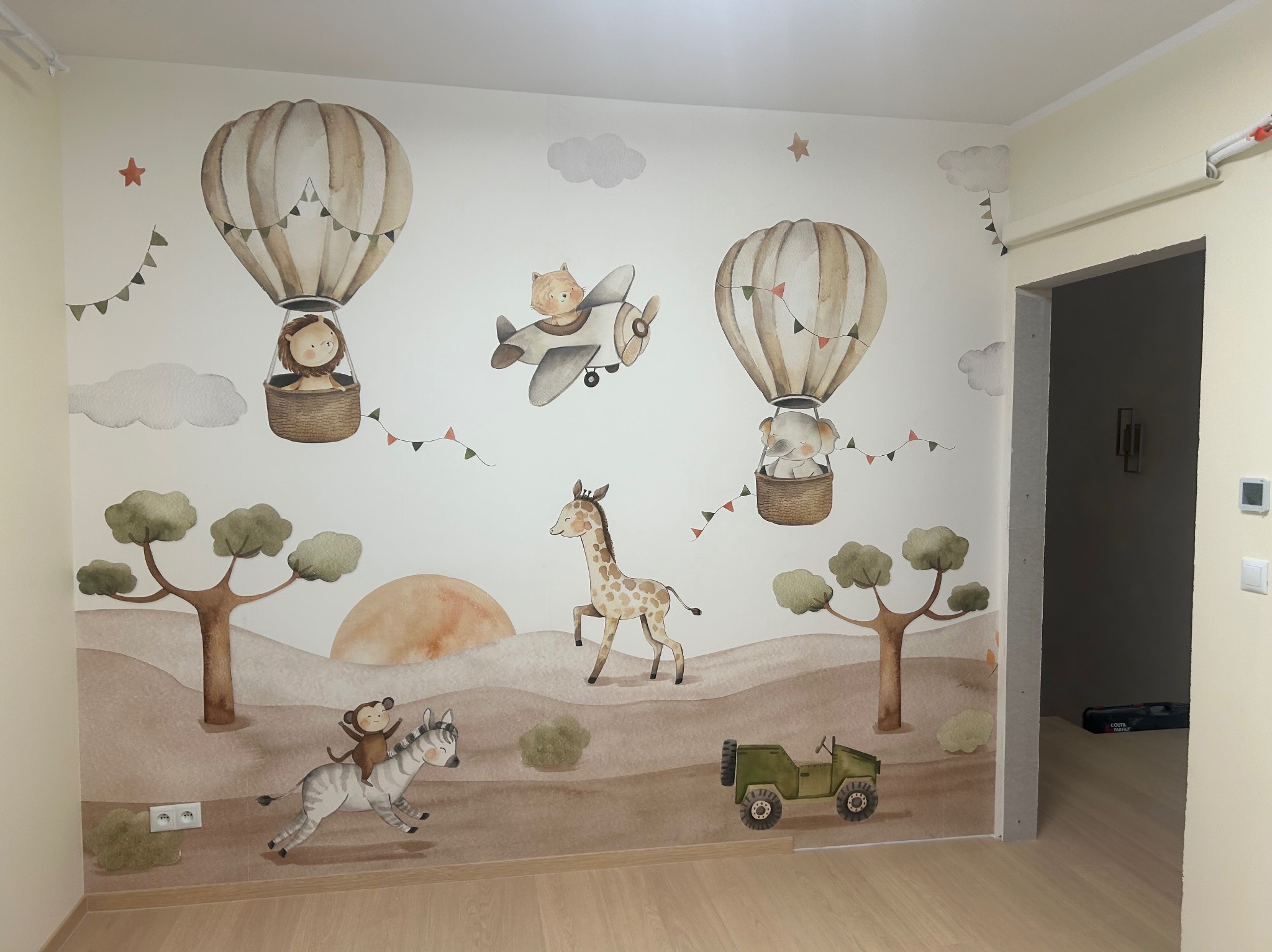 Dziecięcy pokój z tapetą w stylu safari: żyrafa, zebra z małpką, balon, samolot i jeep na tle wzgórz i drzew. Pastelowe kolory, akwarelowy efekt.