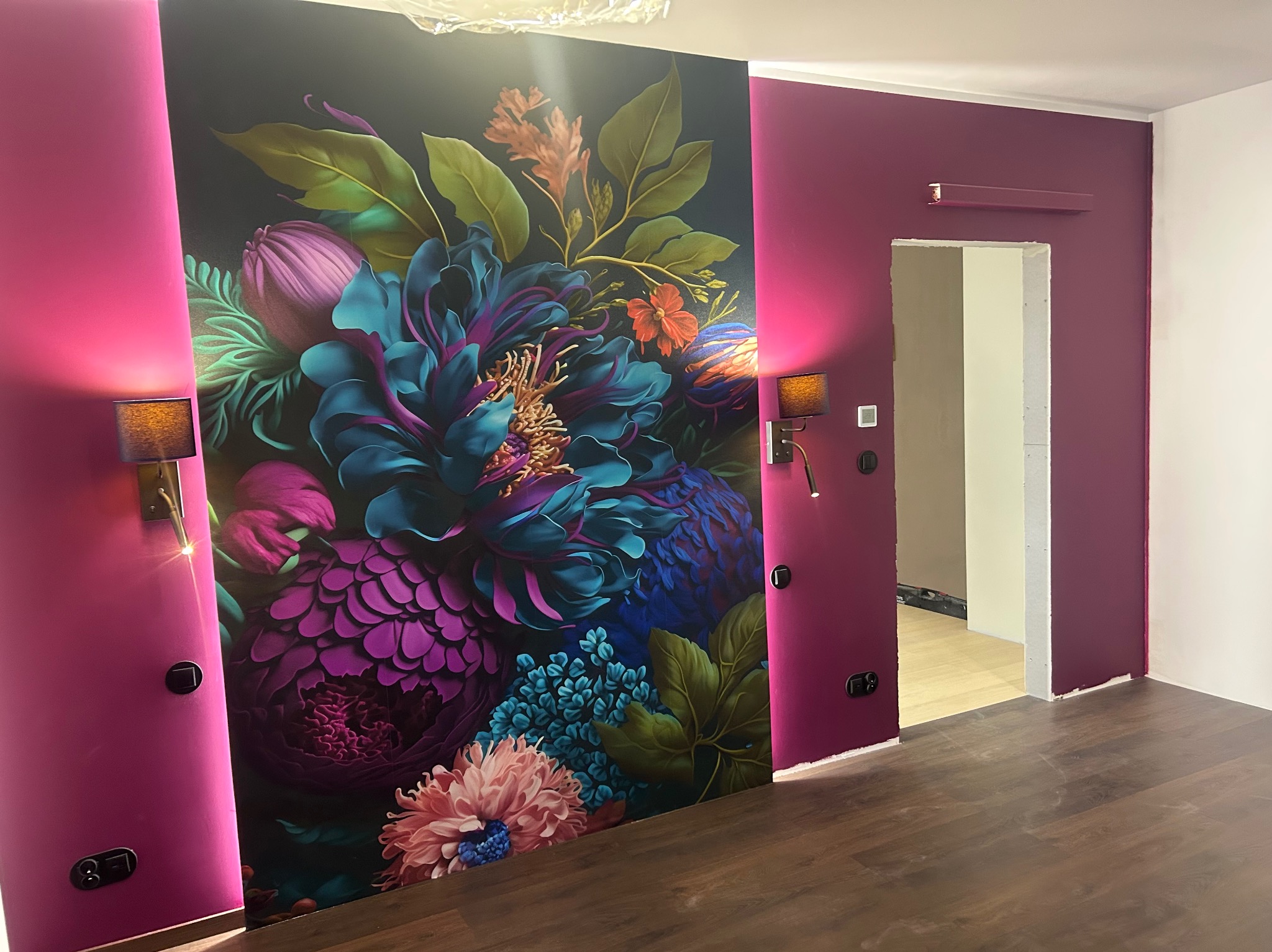 Kwiatowa fototapeta na ścianie w Markach, oświetlona kinkietami, tworzy unikalny akcent w pomieszczeniu z bordowymi ścianami i drewnianą podłogą.