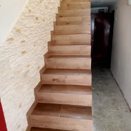 Schody wyłożone płytkami imitującymi drewno, przylegające do ściany z dekoracyjną okładziną kamienną w Krosno. Widoczny fragment korytarza z drzwiami.