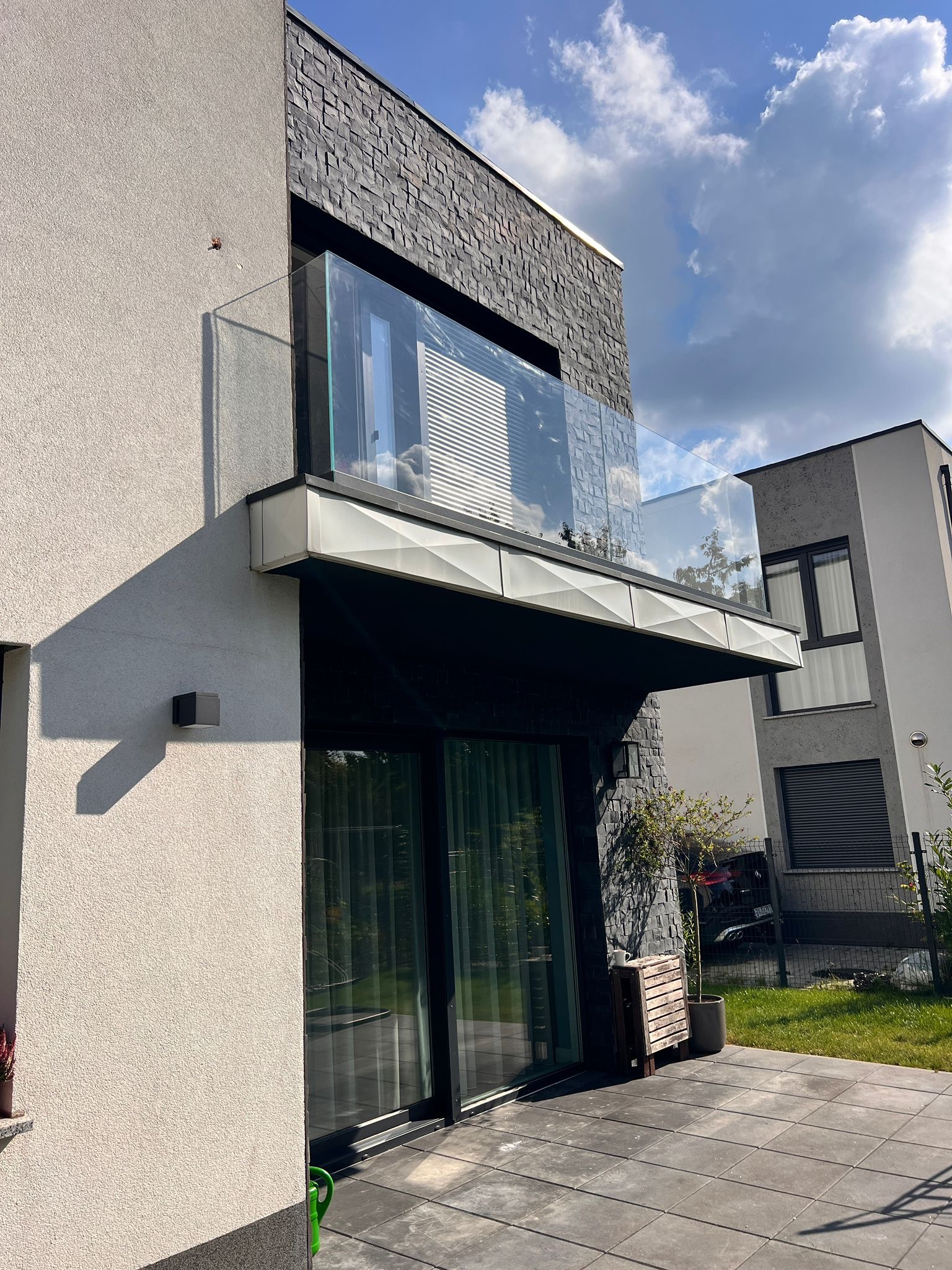 Nowoczesny balkon z szklaną balustradą, widok z dołu, podkreślający minimalistyczny design i użycie szkła. Eleganckie wykończenie budynku z elementami kamiennymi.