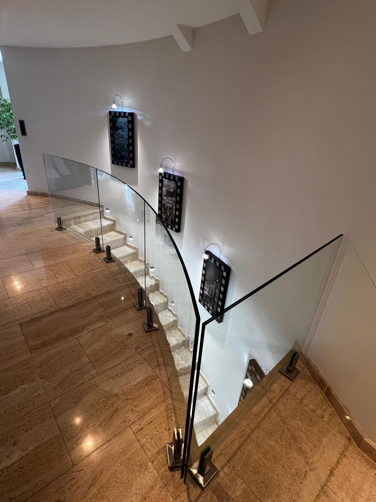 Elegancka, zakrzywiona balustrada ze szkła i czarnych elementów mocujących, zamontowana na marmurowych schodach w jasnym wnętrzu. Widok z góry.