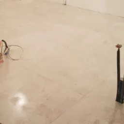 Ułożona, jasna, kwadratowa podłoga z płytek ceramicznych z widocznymi rurami instalacji wodnej i zwiniętym kablem elektrycznym oraz pojemnikiem z narzędziami.