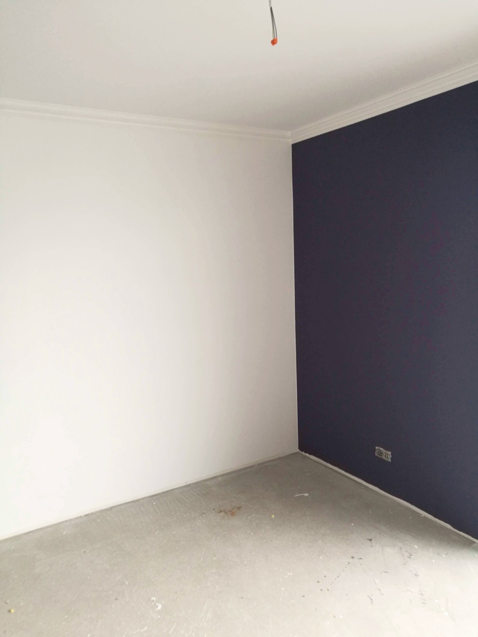 Pomieszczenie po częściowym pomalowaniu ścian na biało i granatowo, widoczna listwa przysufitowa i niedokładności na podłodze.