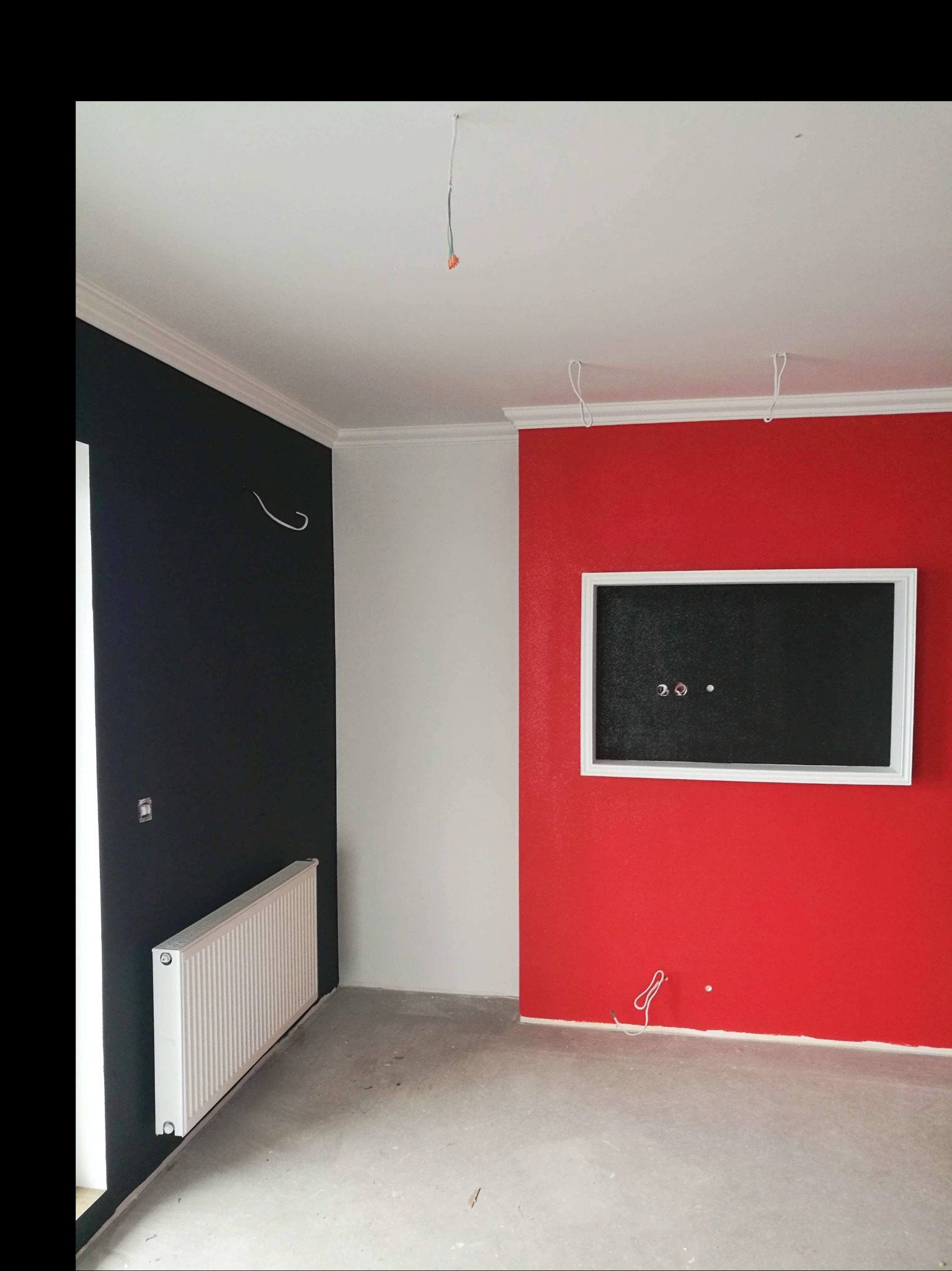 Pokój w Parczewie po częściowym malowaniu ścian na czarno i czerwono, z widocznymi listwami przysufitowymi, grzejnikiem i przygotowanym miejscem na telewizor.