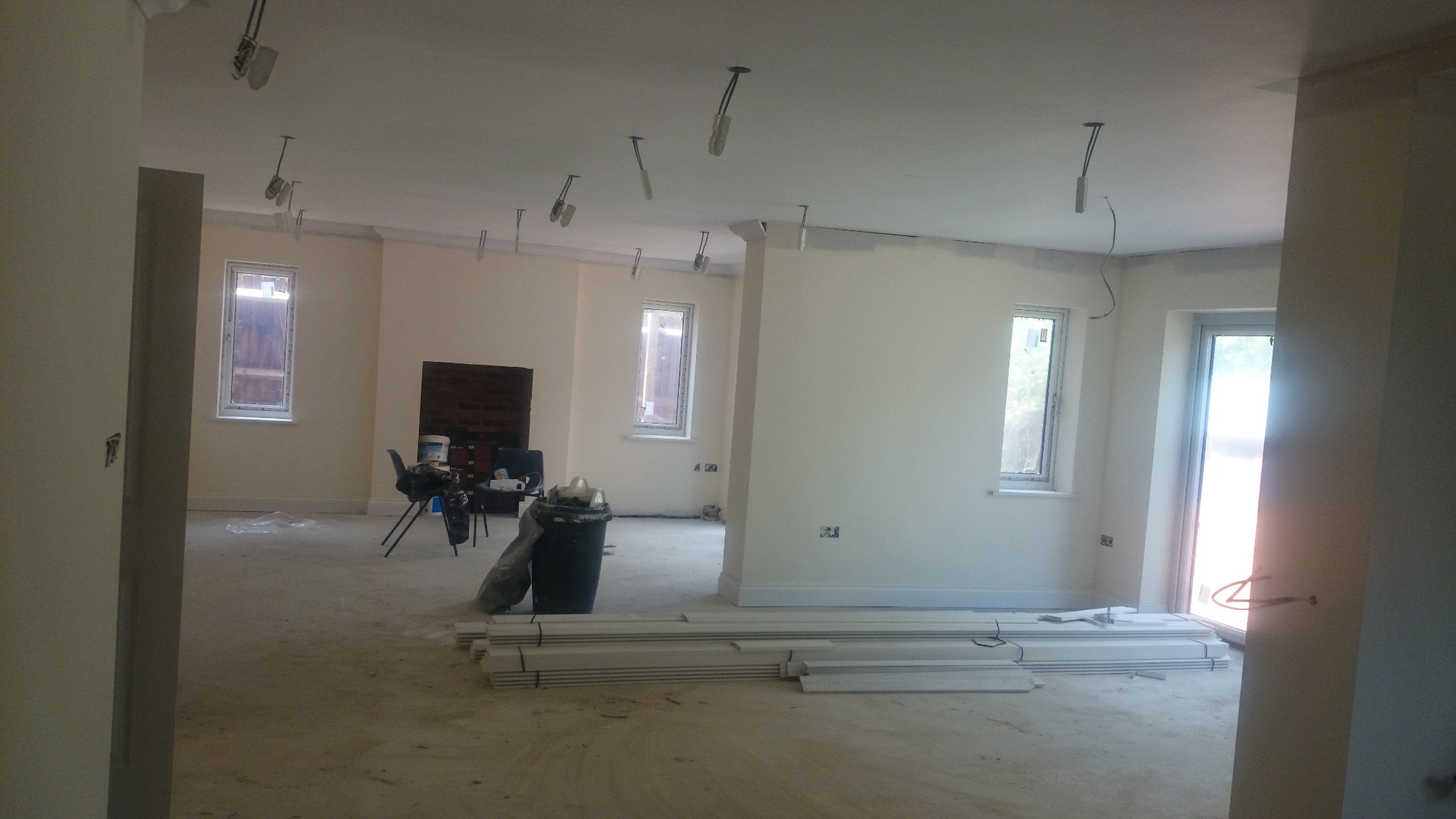 Wnętrze w trakcie malowania ścian na jasny kolor, widoczne listwy przypodłogowe, przygotowane do montażu, oraz instalacje elektryczne pod sufitem