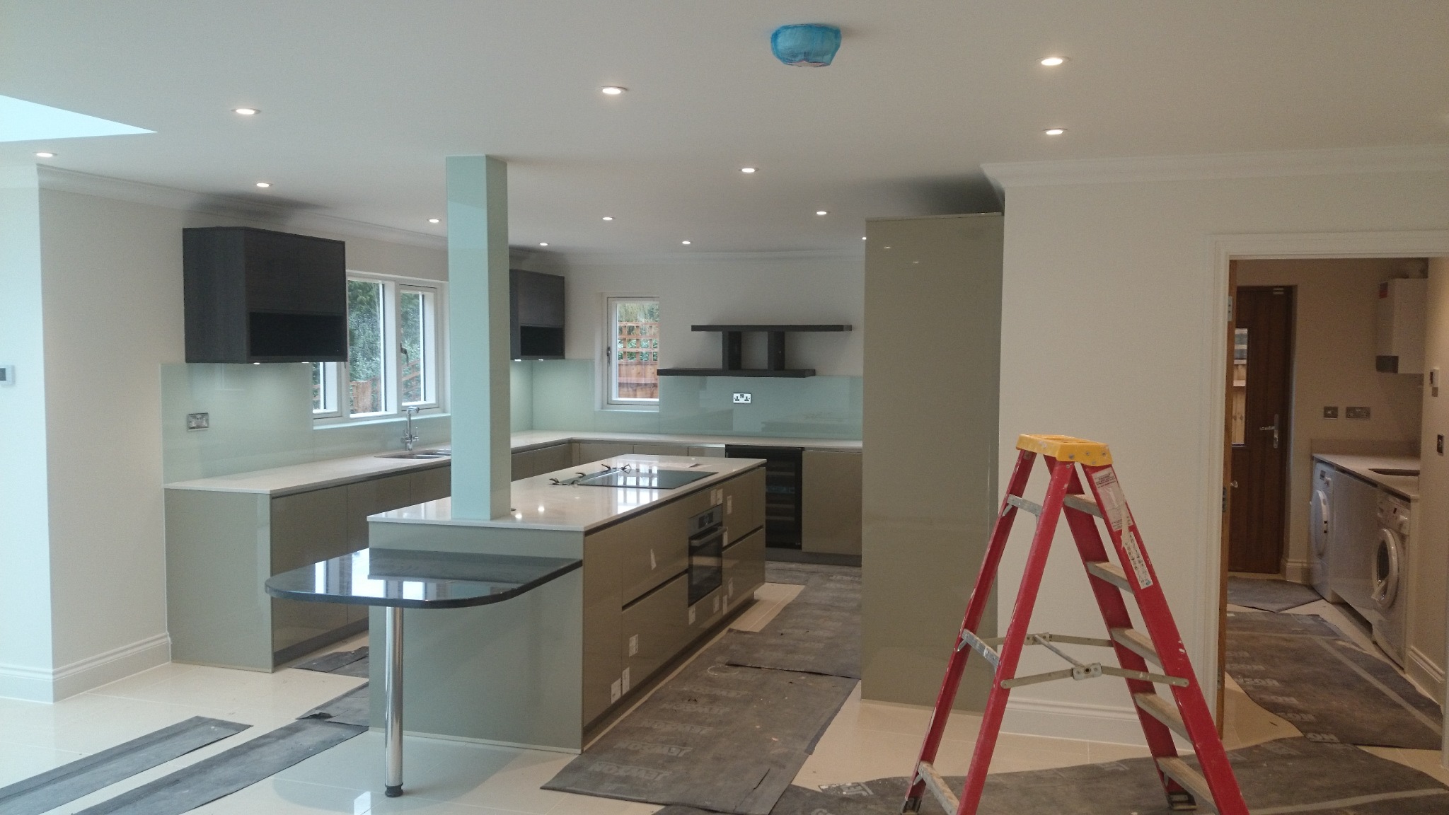 Wnętrze nowoczesnej kuchni w trakcie remontu, widoczna drabina malarska, zabezpieczona podłoga i świeżo pomalowane ściany w odcieniach bieli i szarości.