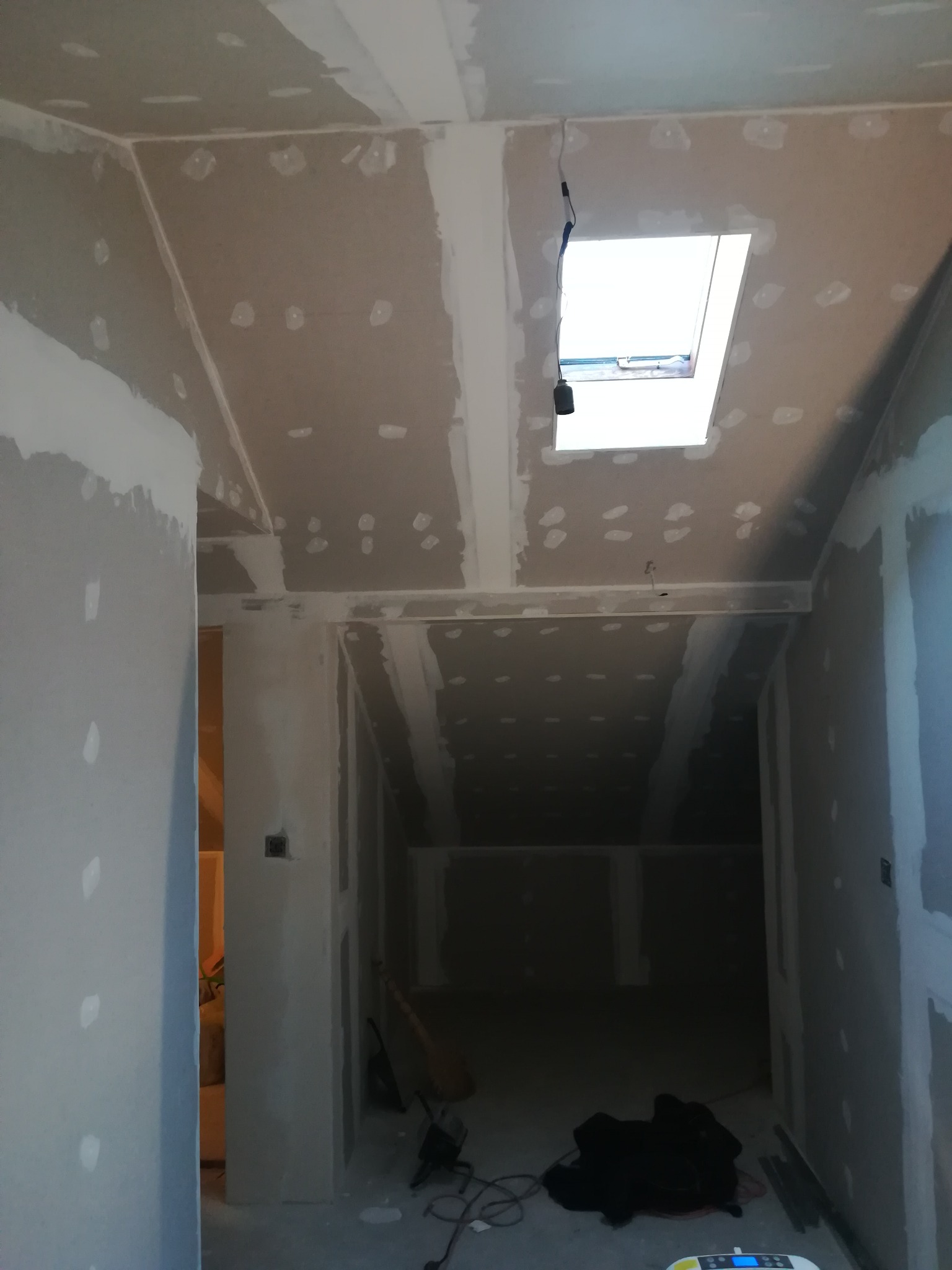 Wnętrze w trakcie montażu płyt karton gips z widocznym oknem dachowym i szpachlowanymi łączeniami.