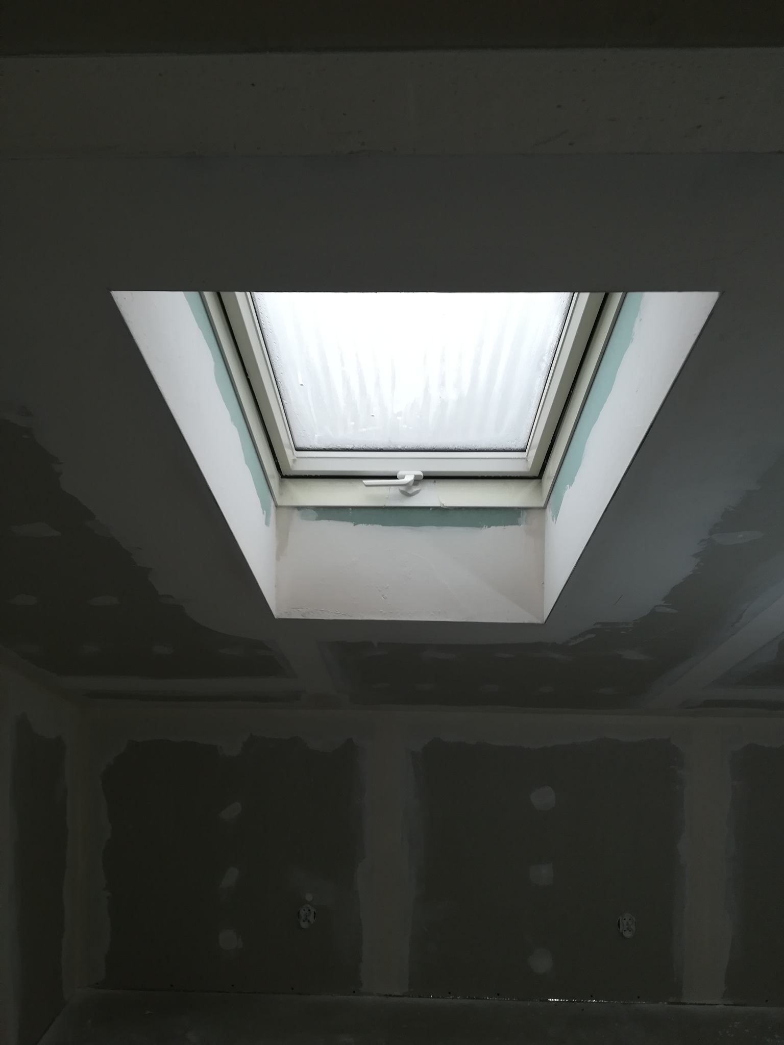 Montaż okna dachowego w suficie z płyt kartonowo-gipsowych, widoczne szpachlowanie łączeń.