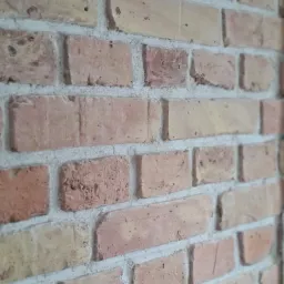 Ściana z cegły klinkierowej w odcieniach beżu i czerwieni, z widoczną fakturą i fugami. Ujęcie z bliska, lekko z boku.