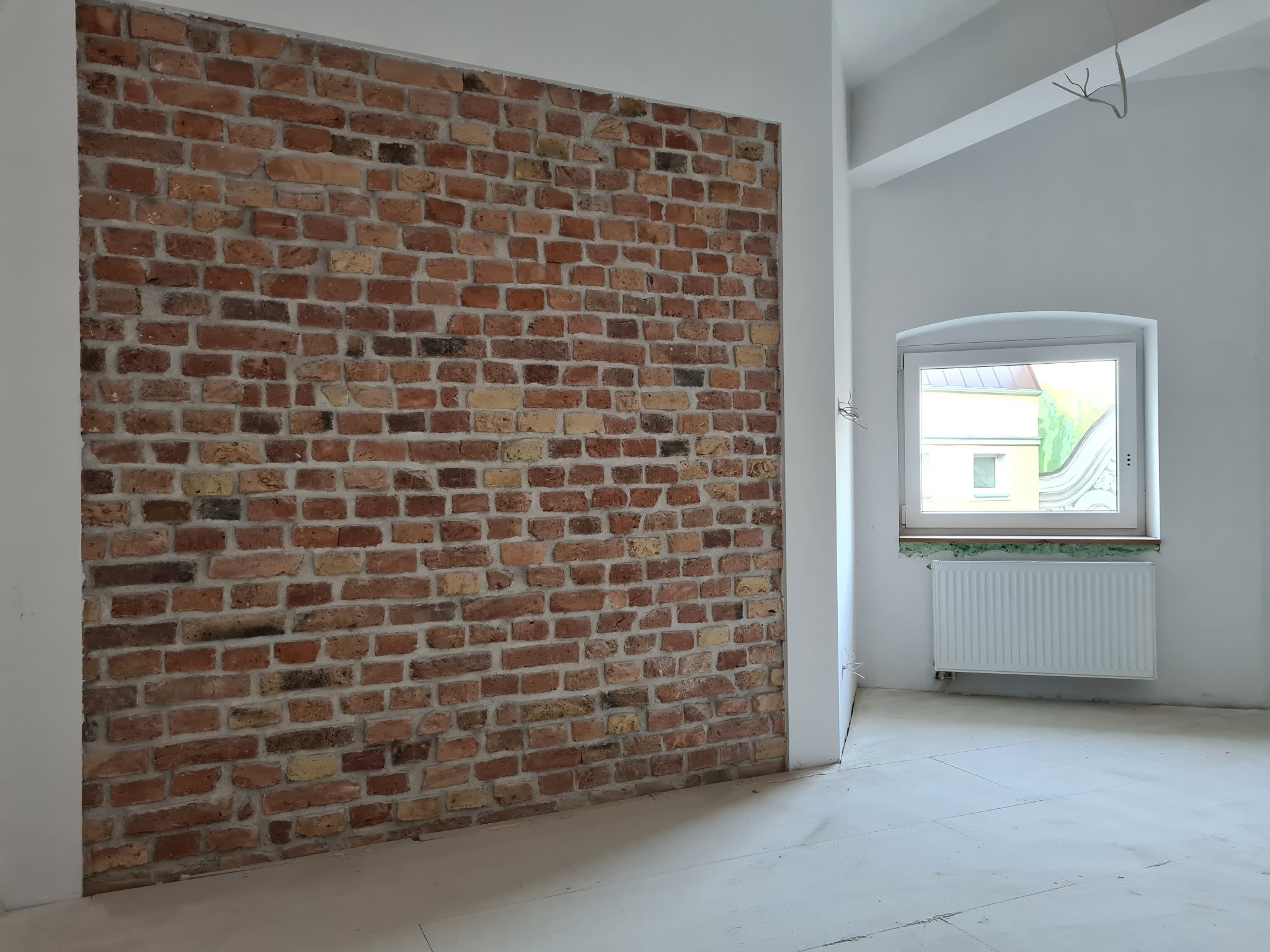 Ściana z cegły rozbiórkowej w surowym wnętrzu, widok na okno z parapetem z zieloną izolacją