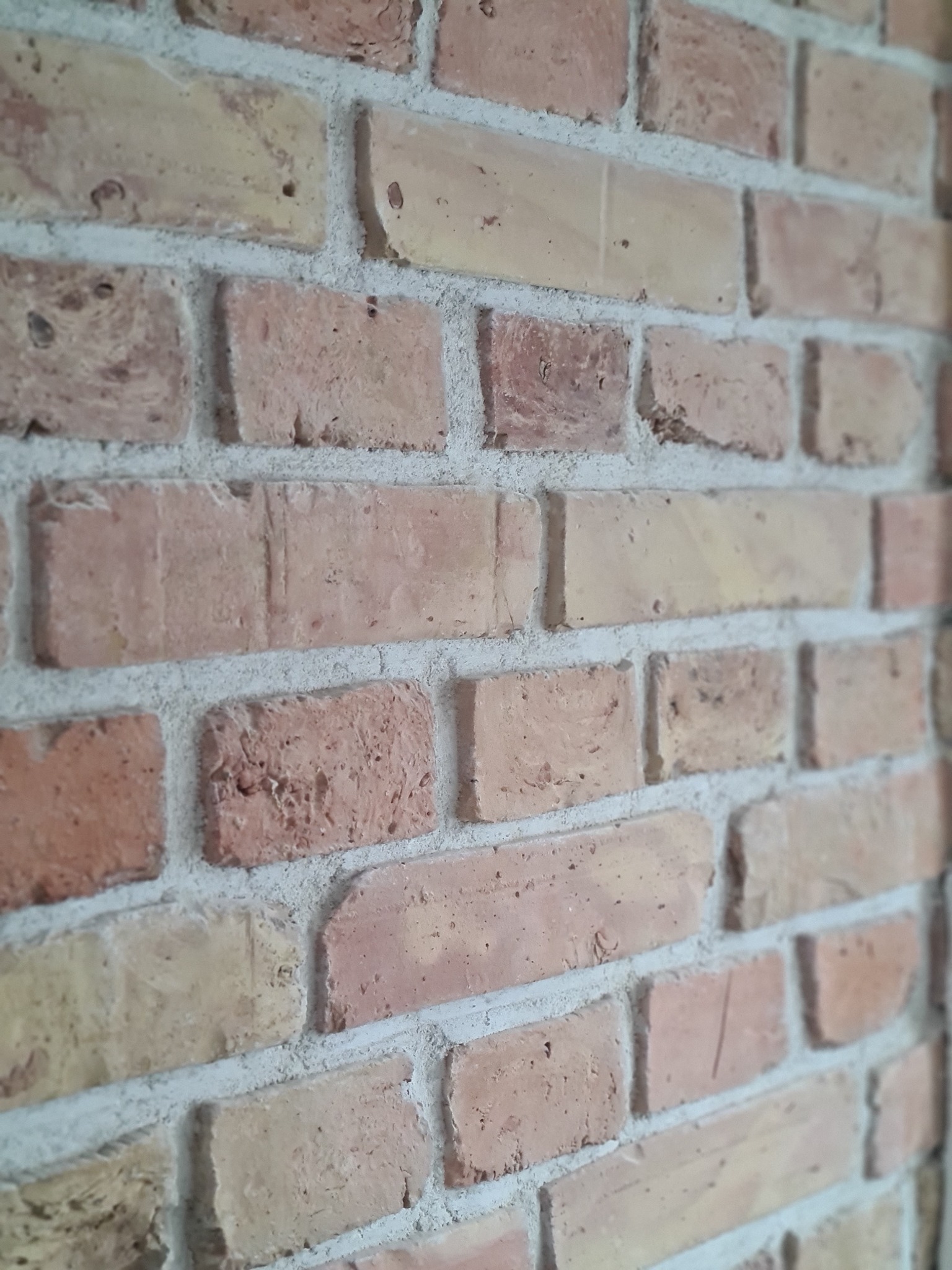 Ściana z cegły klinkierowej w odcieniach beżu i czerwieni, z widoczną fakturą i fugami. Ujęcie z bliska, lekko z boku.
