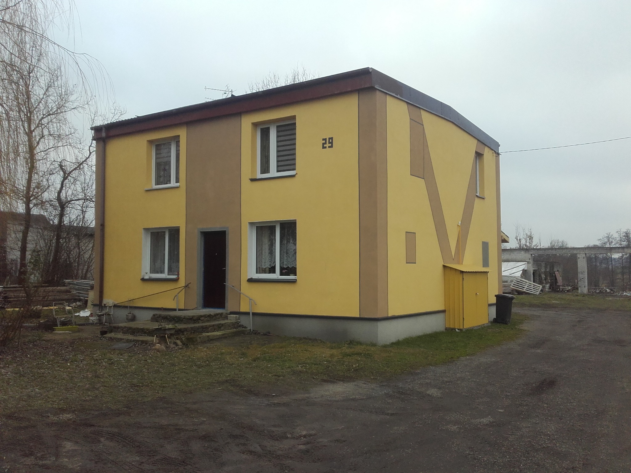Dwukondygnacyjny budynek po ociepleniu elewacji, z żółtą fasadą i brązowymi akcentami, numer 29 na ścianie, widoczne pozostałości po budowie w tle.