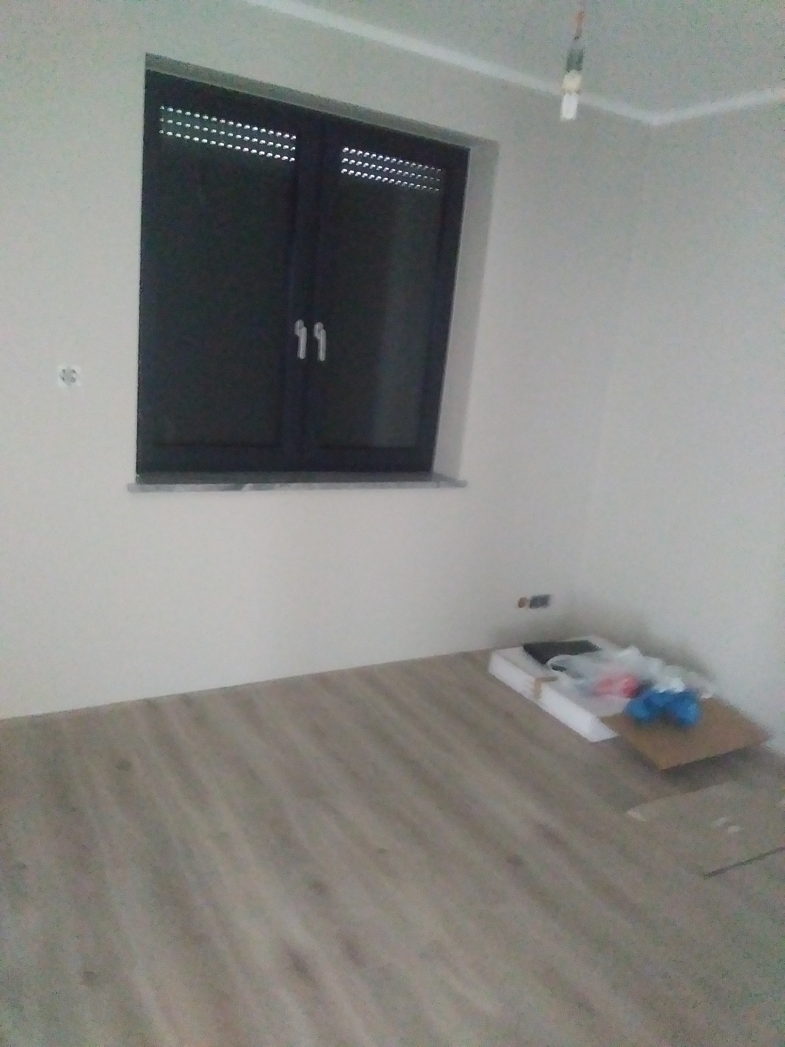 Ułożone panele podłogowe w jasnym odcieniu drewna w pokoju z czarnym oknem w Namysłowie, widoczne materiały budowlane w rogu pomieszczenia.