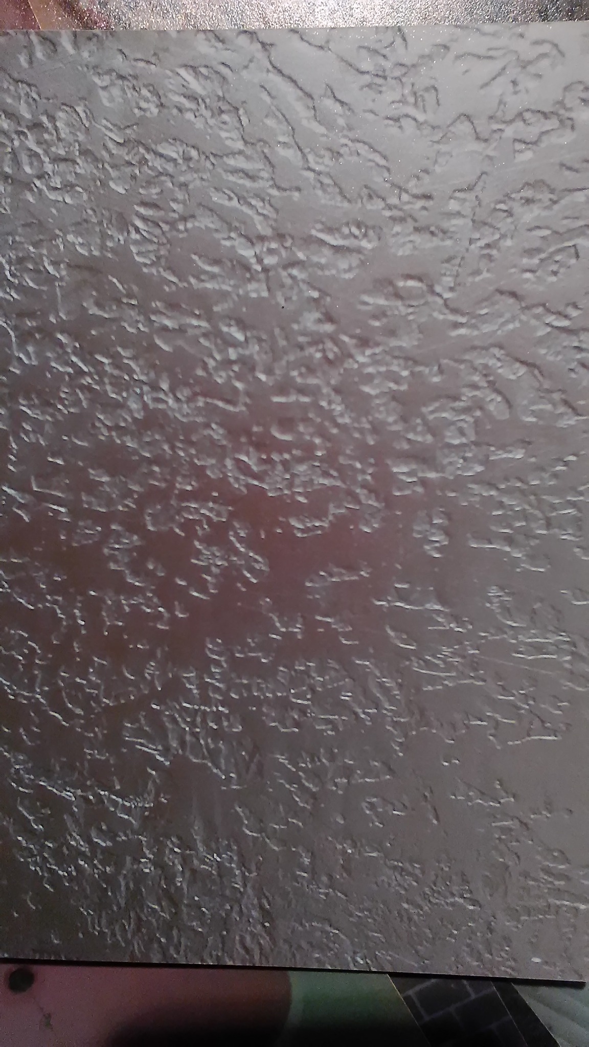 Szara, strukturalna powierzchnia z wyraźnym wzorem przypominającym popękany grunt. Delikatny połysk podkreśla nierówności. Widoczne krawędzie arkusza.