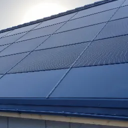 Nowoczesny dach z panelami fotowoltaicznymi w kolorze grafitowym, widok z dołu ukazujący precyzyjne połączenia i minimalistyczny system orynnowania.