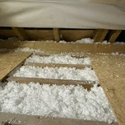 Poddasze w trakcie ocieplania wełną mineralną, widoczne krokwie drewniane i płyty OSB, częściowo wypełnione izolacją.