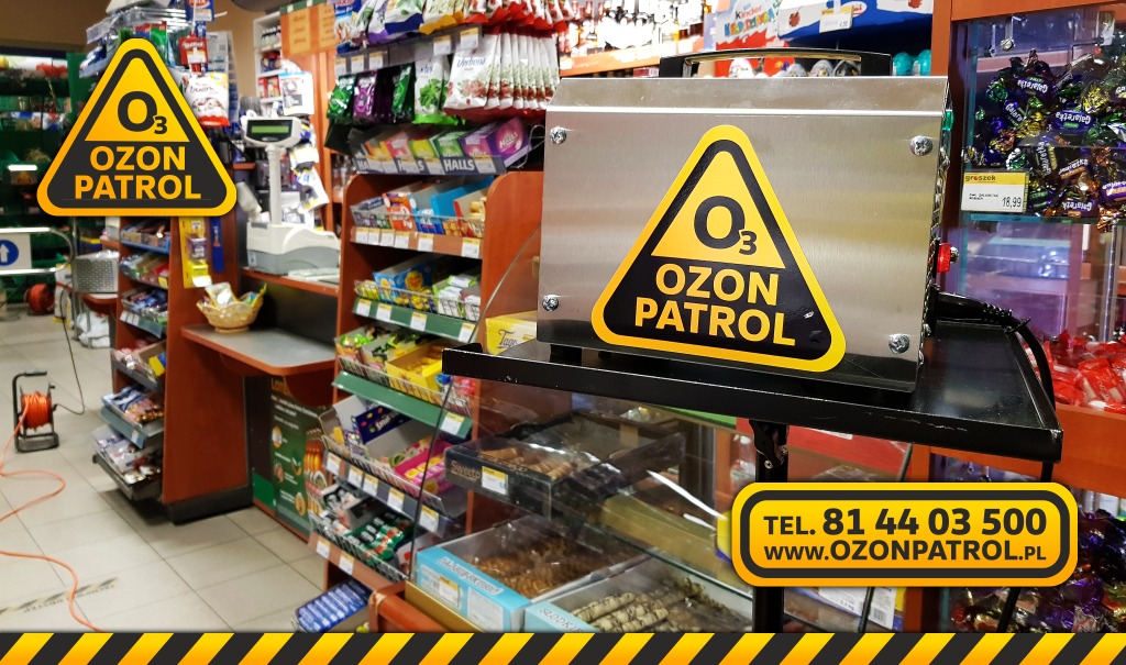 Urządzenie do ozonowania 'Ozon Patrol' ustawione na półce w sklepie, widoczne słodycze i przekąski w tle. Kabel urządzenia zwinięty na podłodze.