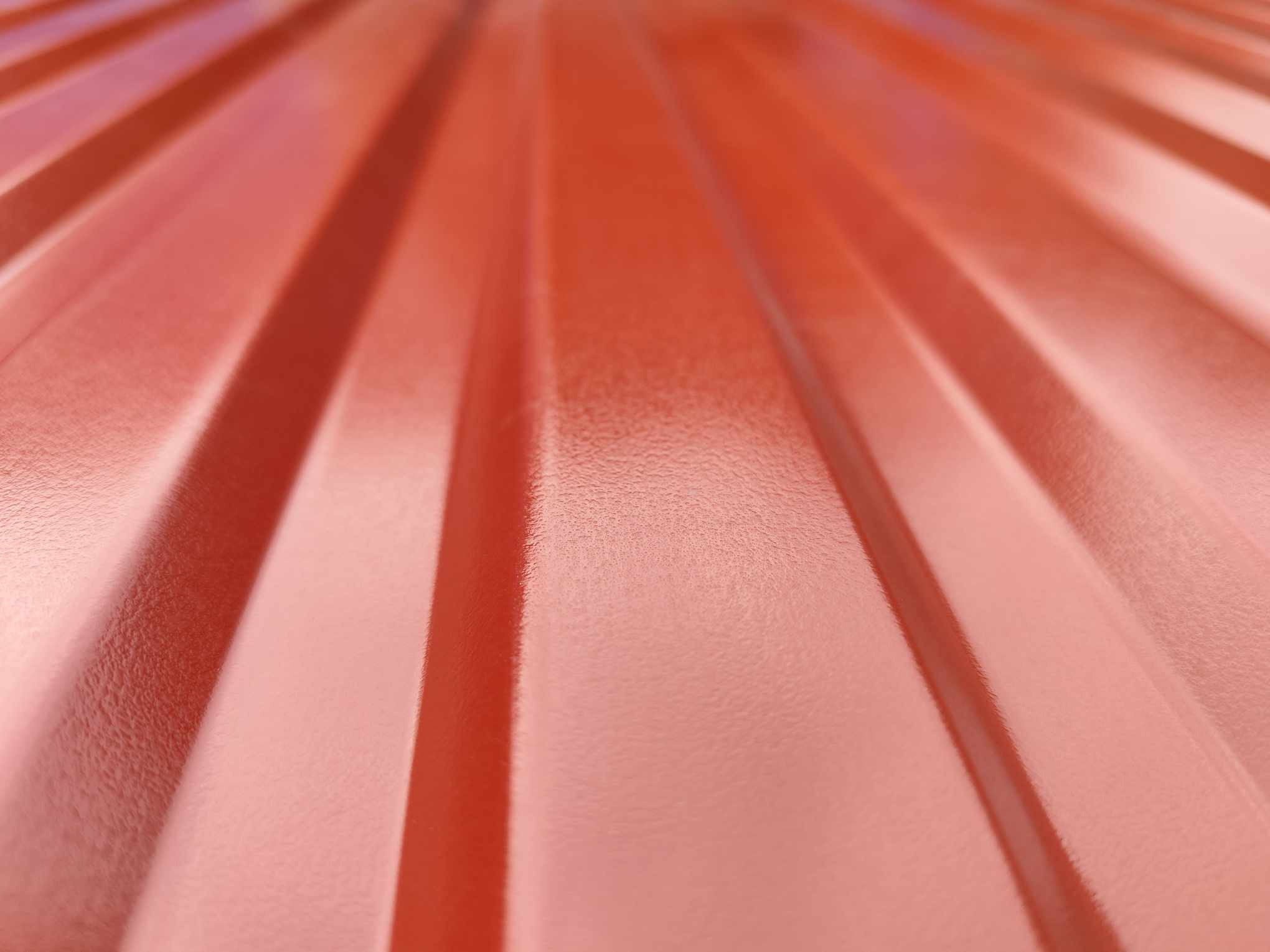 Czerwona blacha o trapezowym profilu, widoczna z bliska pod kątem, ukazująca teksturę i odbicia światła.