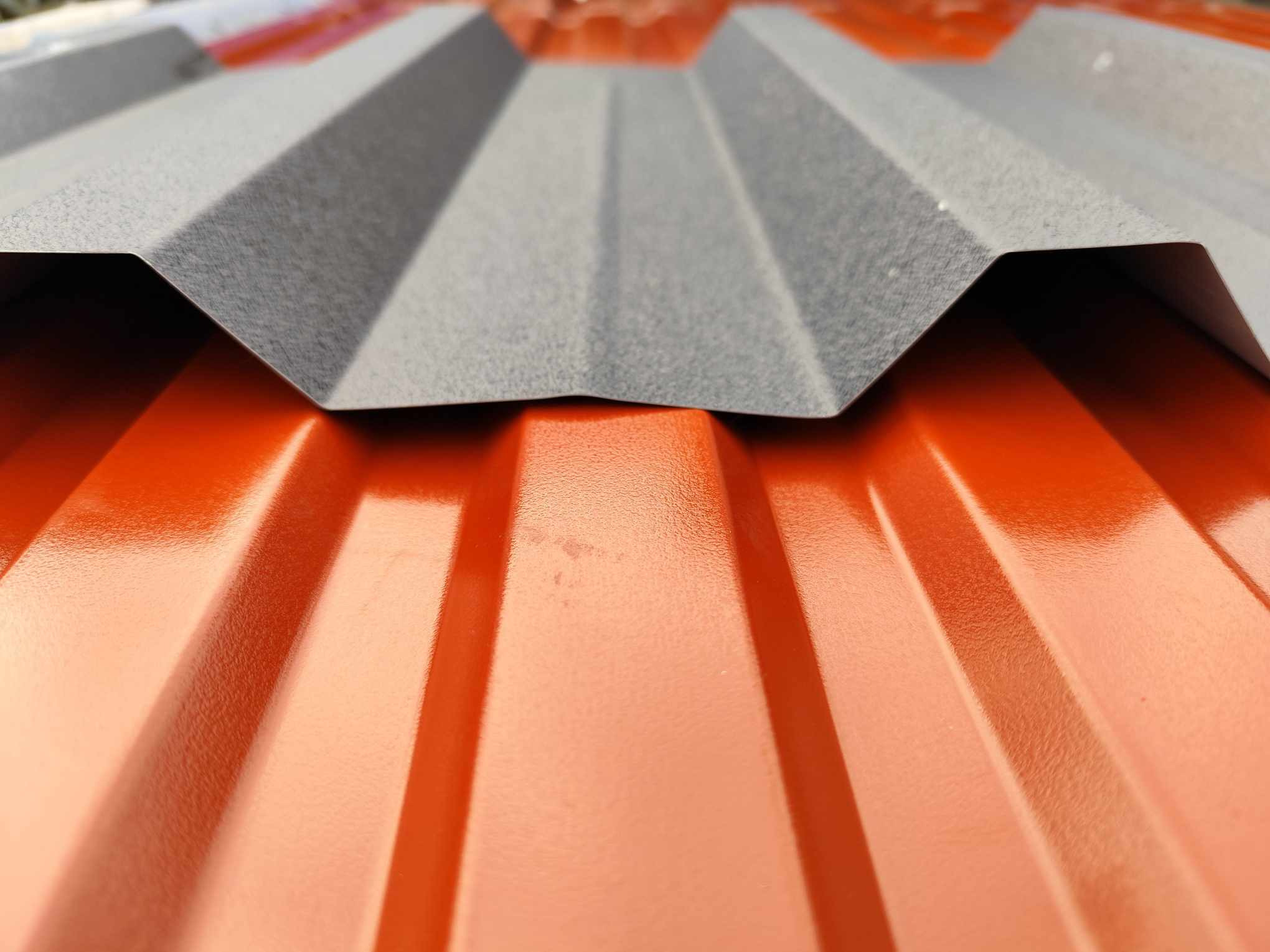 Detale łączenia blachy trapezowej w kolorach ceglastym i szarym, widoczne żłobienia i faktura materiału.