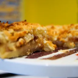 Kawałek domowej szarlotki z kruszonką, widoczny przekrój z nadzieniem jabłkowym na talerzu z brązowymi paskami.