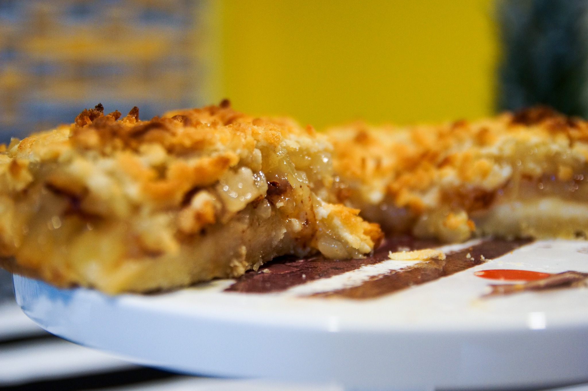 Kawałek domowej szarlotki z kruszonką, widoczny przekrój z nadzieniem jabłkowym na talerzu z brązowymi paskami.