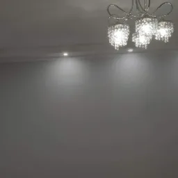 Świeżo pomalowane na szaro ściany z listwami przysufitowymi i punktowym oświetleniem oraz ozdobnym żyrandolem w wykończonym pokoju.