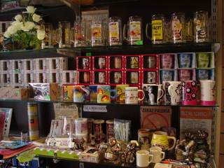 Wnętrze sklepu z pamiątkami w Katowicach: półki uginają się pod ciężarem kubków, kufli, figurek i innych drobiazgów, kwiaty w wazonie dodają uroku, a tabliczki informacyjne regulują zasady.