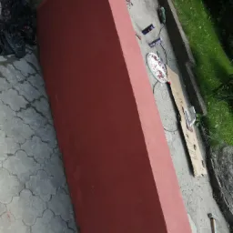 Czerwona ściana z narzędziami budowlanymi obok, w tym szlifierka kątowa, puszki, kielnia i młotek na zewnątrz.