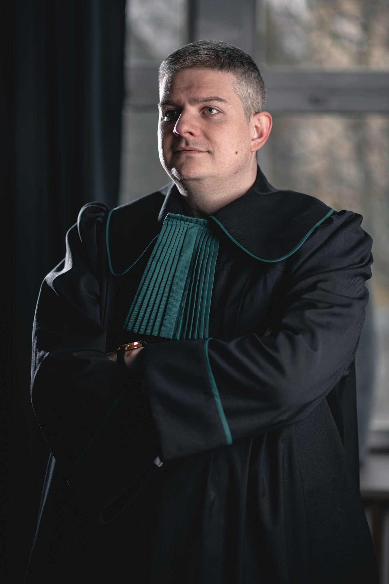 Portret mężczyzny w todze adwokackiej z zielonym żabotem, z założonymi rękami na tle okna.