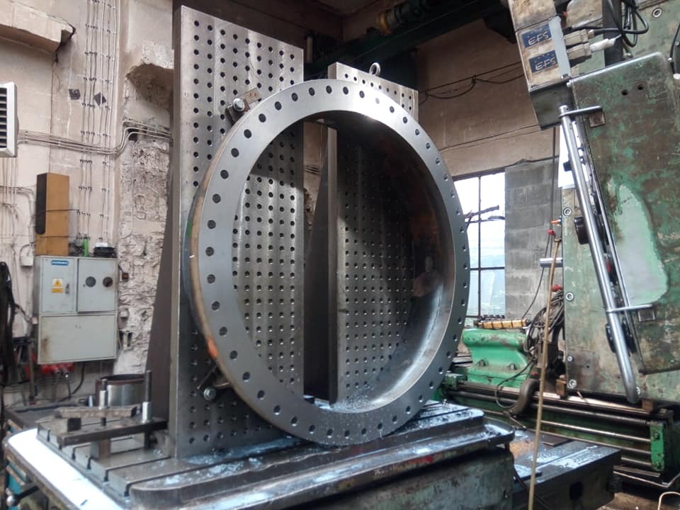 Obróbka metalowego pierścienia z otworami na frezarce CNC; widoczny uchwyt mocujący i chłodziwo.