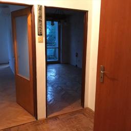 SW Projekt - Wnętrze mieszkania w Malborku z widocznymi parkietami w jodełkę, otwarte drzwi z szybą i widok na balkon zza kolejnych drzwi.