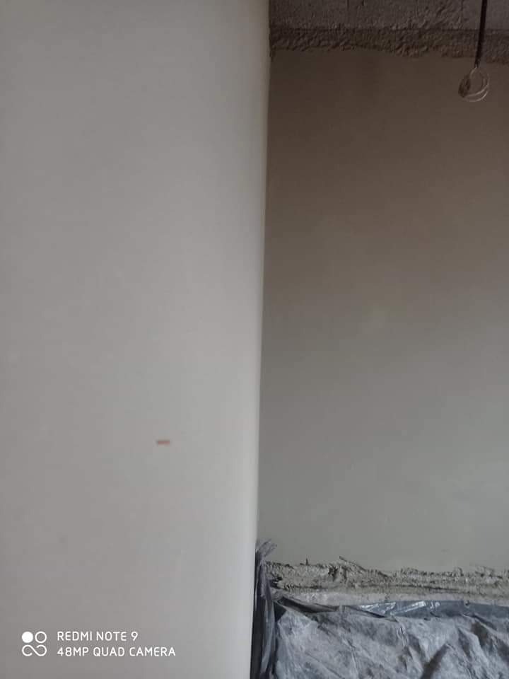 Świeżo otynkowana ściana wewnętrzna w trakcie schnięcia, zabezpieczona folią ochronną u dołu, widoczne niedoskonałości surowego tynku przy suficie.