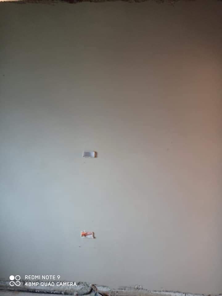 Świeżo otynkowana ściana z widocznymi puszkami elektrycznymi, przygotowana do dalszych prac wykończeniowych.