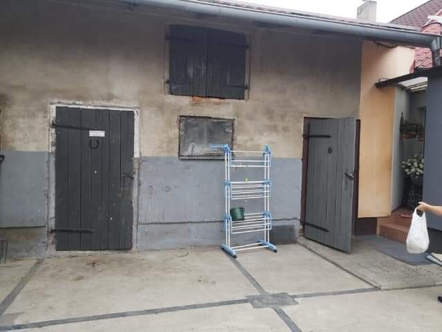 Szara ściana budynku gospodarczego z dwiema drewnianymi bramami, oknem z okiennicami i suszarką na pranie