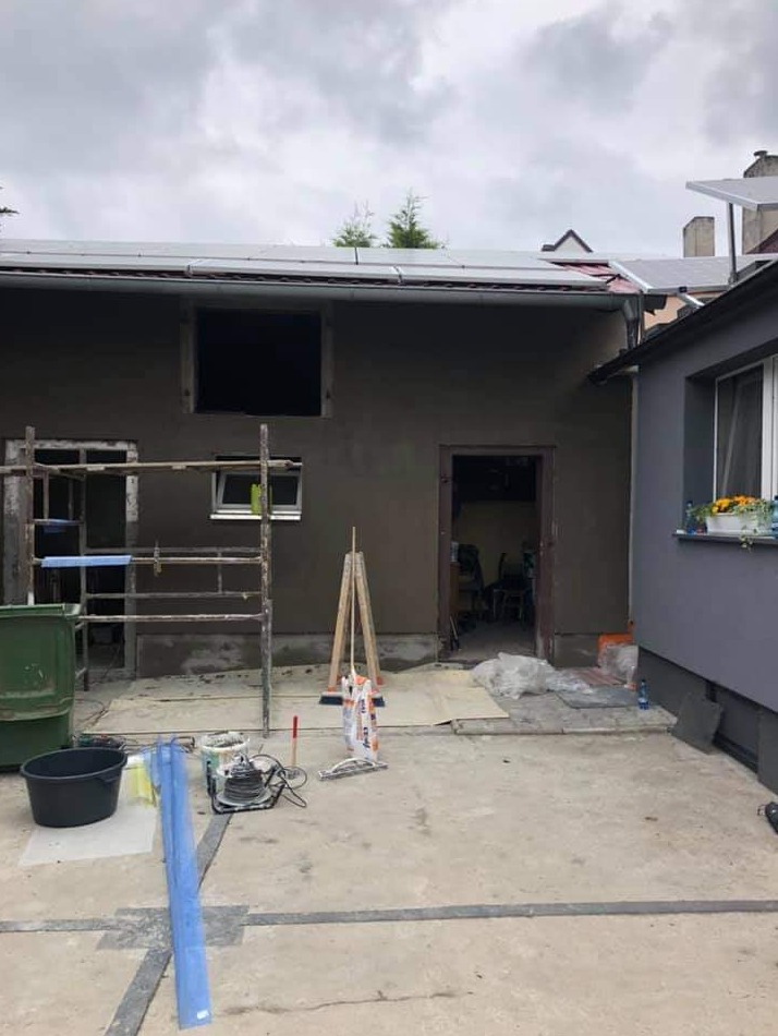 Elewacja budynku po nałożeniu tynku maszynowego, widoczne rusztowanie, narzędzia i worki z zaprawą, przygotowane do dalszych prac wykończeniowych.