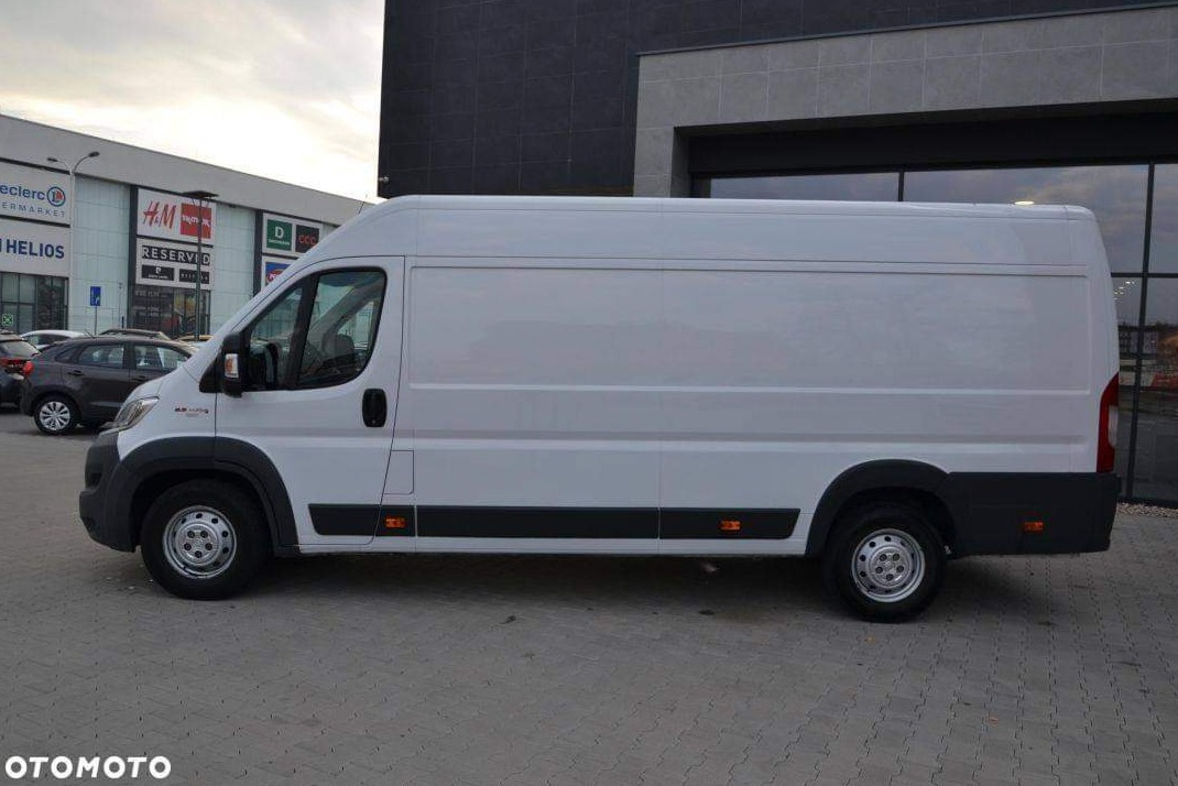 Biały samochód dostawczy na tle budynku centrum handlowego, widok z boku.