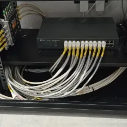 Szafa rack z zamontowanym switchem sieciowym TP-Link i patch panelem Televes, okablowanie strukturalne z żółtymi oznaczeniami, widoczne kable Ethernet.