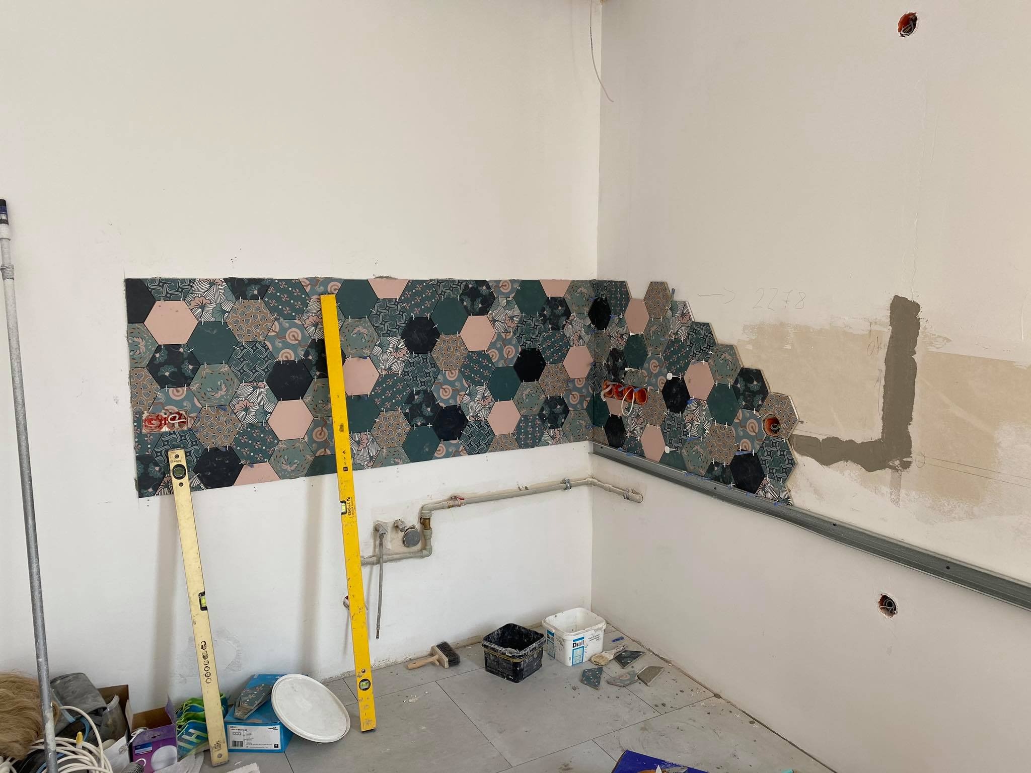 Układanie dekoracyjnych heksagonalnych płytek na ścianie w kuchni w Warszawie, widoczne poziomice i narzędzia glazurnicze, fragment ściany przygotowany pod dalsze płytki.