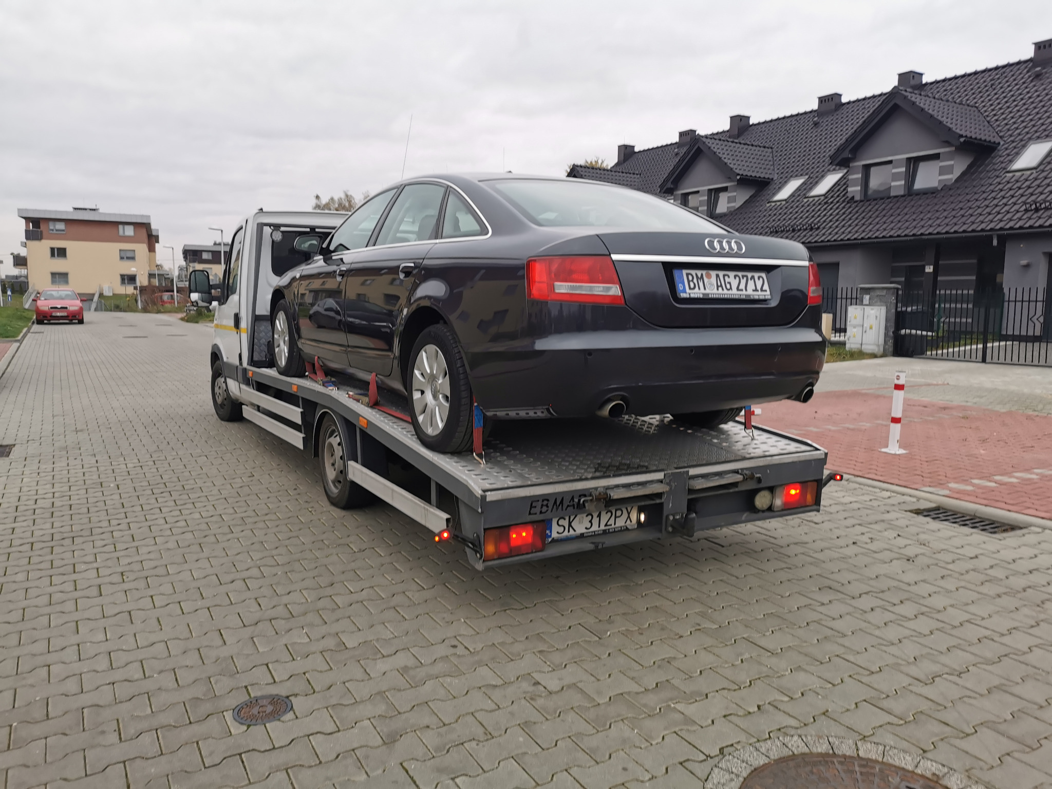 Czarny samochód osobowy marki Audi z niemiecką tablicą rejestracyjną transportowany na lawecie w zabudowie miejskiej.
