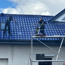 Roofers Folding Group - Dwóch pracowników na rusztowaniu czyści niebieski dach domu za pomocą myjki ciśnieniowej, widoczne ślady spływającej wody na elewacji.