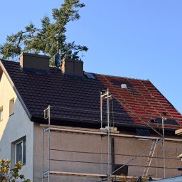 Roofers Folding Group - Dom z częściowo zdjętym, czerwonym poszyciem dachu, obok fragmentu z brązową dachówką. Widoczne rusztowanie i kominy. Prace dekarskie w toku.