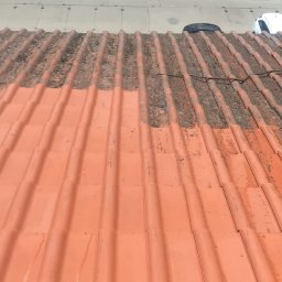 Roofers Folding Group - Częściowo oczyszczony dach z czerwonej dachówki, widoczne zabrudzenia i mech po jednej stronie, czysta powierzchnia po drugiej. Prace w toku.