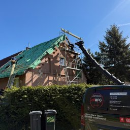 Roofers Folding Group - Dom w trakcie krycia dachu, widoczne rusztowania, ekipa dekarzy i zsyp gruzu. Na pierwszym planie samochód firmy dekarskiej.