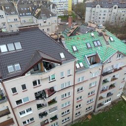 Roofers Folding Group - Wielorodzinny budynek z częściowo wymienionym dachem: ciemna dachówka po lewej, zielona membrana i łaty pod dachówkę po prawej. Widoczne okna dachowe i inne budynki w tle.