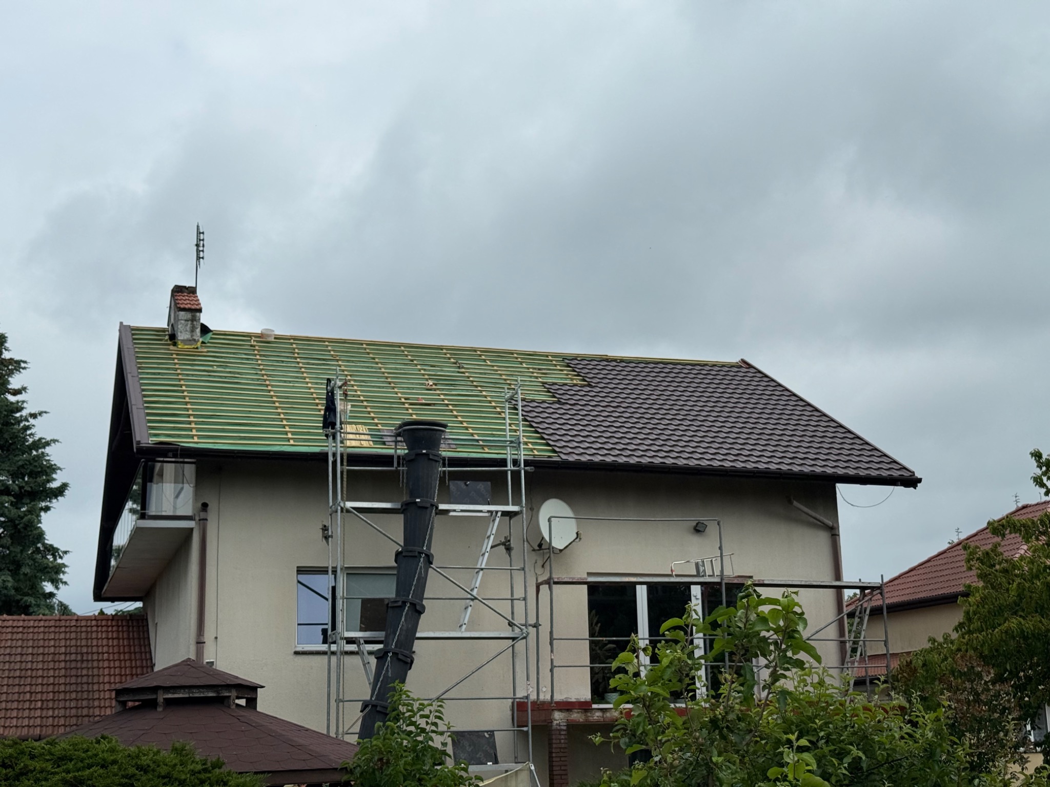 Dom w Szczecinie z częściowo wymienionym dachem, widoczne rusztowania i elementy konstrukcyjne dachu przed położeniem nowego pokrycia. Część dachu pokryta brązową dachówką.