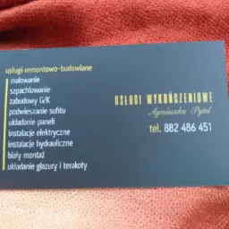 Wizytówka firmy remontowo-budowlanej 'Usługi Wykończeniowe Agnieszka Pytel' z numerem telefonu 882 486 451, leżąca na pomarańczowej tkaninie. Oferta obejmuje malowanie, szpachlowanie, zabudowy G/K,...